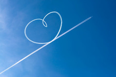 飞机飞行通过清晰的蓝色的天空左心形状蒸汽小径的背后心形状的天空从的飞机痕迹