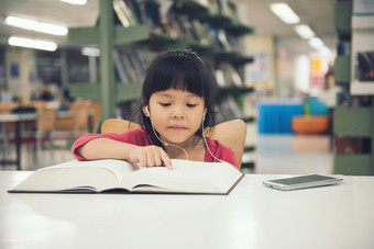 可爱的小孩子们女孩研究读书的图书馆房间和书架子上背景孩子们听首歌音乐从智能手机表格