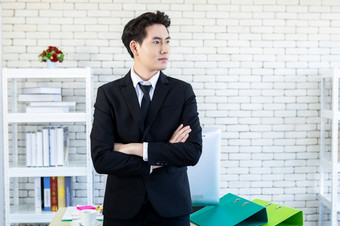 肖像快乐的成熟的亚洲年轻的商人穿业务西装男人。蓝色的夹克和蓝色的衬衫看的窗口的办公室房间背景