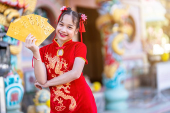 肖像美丽的微笑可爱的小亚洲女孩穿红色的传统的中国人旗袍装饰持有黄色的信封手为中国人新一年节日中国人神社