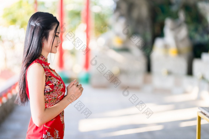 美丽的亚洲年轻的女人穿红色的传统的中国人旗袍装饰坐着为祈祷佛雕像为中国人新一年节日中国人神社泰国
