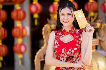 肖像美丽的微笑亚洲年轻的女人穿红色的传统的中国人旗袍装饰持有黄色的信封手为中国人新一年节日中国人神社泰国