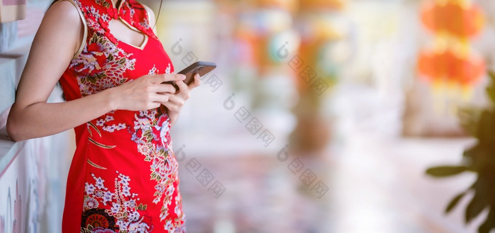 关闭亚洲年轻的女人穿红色的传统的中国人旗袍装饰和写作消息智能手机为中国人新一年节日中国人神社泰国