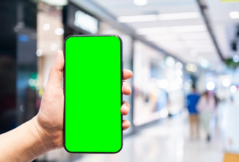 特写镜头女使用手持有智能手机与空空白绿色屏幕模糊图片触摸摘要模糊内部购物复杂的背景购物在线概念