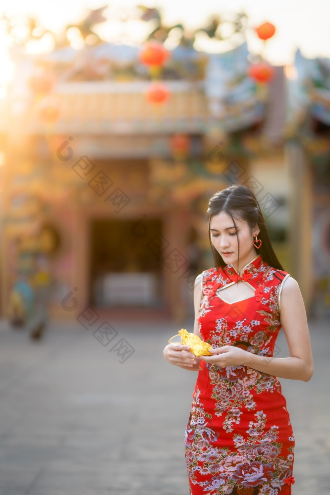 肖像美丽的微笑亚洲年轻的女人穿红色的传统的中国人旗袍装饰持有金钱袋为中国人新一年节日中国人神社泰国
