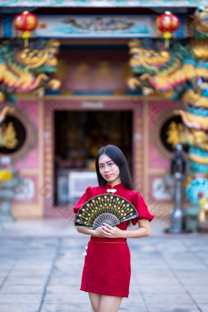 肖像美丽的微笑亚洲年轻的女人穿红色的传统的中国人旗袍装饰和持有中国人范宁为中国人新一年节日中国人神社泰国