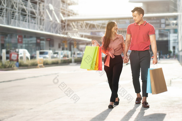 快乐年轻的夫妇购物者走的购物街对和持有色彩斑斓的购物袋手概念出售和黑色的星期五购物