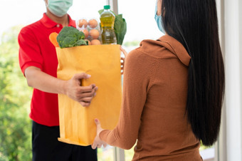 亚洲交付男人。从超市穿脸面具和持有袋新鲜的食物蔬菜和水果为给客户首页概念表达杂货店服务和<strong>新生活</strong>方式