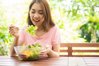 的快乐美丽的亚洲健康的中间岁的女人坐着的阳台的房子旁边的花园和吃健康的绿色沙拉概念健康哪和有营养的食物