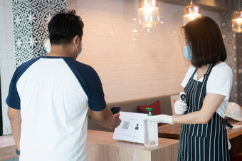 亚洲女服务员女人穿脸面具和持<strong>有</strong>红外温度计和推荐客户使用手酒精洗手液之前<strong>进</strong>入的餐厅咖啡商<strong>店</strong>