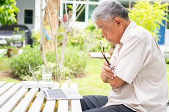 肖像老上了年纪的亚洲男人。使用电脑移动PC的后院为学习新技能后退休概念对老年人的歧视和不晚些时候为学习