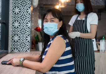 亚洲女人穿面具和坐着咖啡商店和女服务员的面具是服务食物概念新生活方式和<strong>疾病预防</strong>