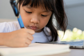 <strong>亚洲女孩</strong>学生持有笔为采取笔记和做家庭作业和使用的移动PC为在线学习类首页教育和距离学习为孩子们在家教育概念