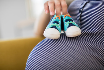 关闭怀孕了女人坐着沙发首页持有婴儿鞋子胃