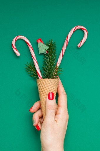 新一年圣诞节圣诞节假期庆祝活动女人手红色的修指甲持有华夫格锥糖果拐杖冷杉树分支复制空间绿色颜色纸背景模板问候卡