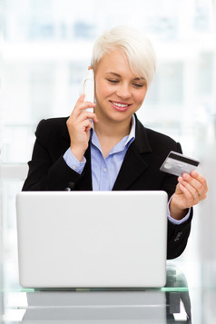 照片金发女郎微笑女人说话电话而在线购物与信贷卡办公室