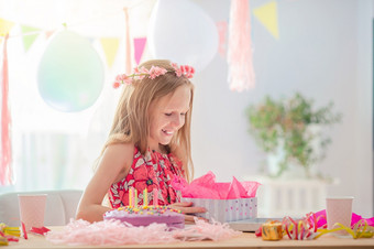 可爱的小女孩拆包现在她的生日孩子快乐和兴奋生日聚会，派对和祝愿概念高加索人女孩如痴如梦微笑和看生日彩虹蛋糕节日色彩斑斓的背景与气球生日聚会，派对和祝愿概念