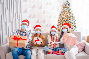 快乐圣诞节家庭四个与礼物圣诞节父母和孩子们是穿口罩快乐年轻的家庭与孩子们持有圣诞节礼物
