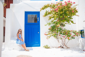 可爱的小女孩衣服老街典型的希腊传统的村与白色墙和蓝色的门可爱的小女孩老街典型的希腊传统的村