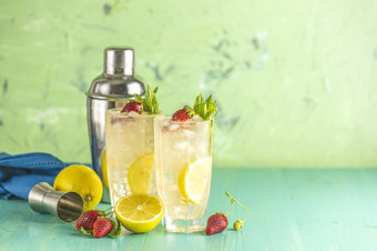 两个眼镜冷冰冷的让人耳目一新喝与柠檬和草莓服务与酒吧工具绿色木表格新鲜的鸡尾酒饮料与冰水果和草装饰