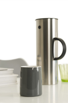 灰色的咖啡杯旁边银真空瓶关闭单灰色的咖啡杯旁边银真空瓶前的表格与白色背景