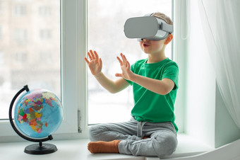 男孩与虚拟现实耳机坐着首页的表格在室内的孩子探讨了的世界虚拟现实通过视频和游戏技术的未来男孩与虚拟现实耳机坐着首页的表格在室内的孩子探讨了的世界虚拟现实通过视频和游戏