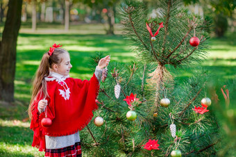 肖像小女孩附近的圣诞节树女孩装修圣诞节树的森林与圣诞节球冬天假期和人概念快乐圣诞节和快乐假期肖像小女孩附近的圣诞节树女孩装修圣诞节树的森林与圣诞节球