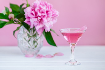 粉红色的牡丹下一个玻璃粉红色的酒粉红色的背景粉红色的牡丹下一个玻璃粉红色的酒