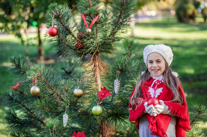 可爱的女孩装修的圣诞节树在户外的院子里之前的假期快乐圣诞节和快乐假期可爱的女孩装修的圣诞节树在户外的院子里之前的假期