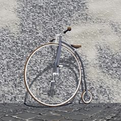 美丽的老灰色自行车与大前面轮和小回来一个对墙的街
