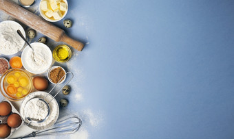 烘焙成分为面团蓝色的背景前视图面粉鸡蛋黄油糖和厨房餐具为自制的烘焙与复制空间为文本烘焙成分蓝色的颜色背景前视图