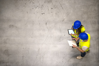 前视图两个工业工人穿安全帽和反光夹克持有平板电脑和检查表灰色的混凝土背景前视图两个工业工人穿安全帽和反光夹克