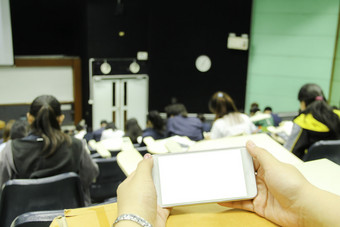 女使用白色移动电话与空白屏幕的教室和模糊背景学生在的研究测试测试考试从老师大讲座房间大学教室