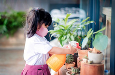 快乐亚洲女孩穿外科手术保护面具而享受花园学校首页孩子学生统一的浇水植物