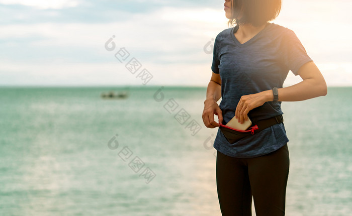 年轻的亚洲女人保持智能手机腰袋之前运行有氧运动锻炼的早....海海滩户外锻炼跑步者和聪明的乐队可穿戴设备小工具为健康的生活方式