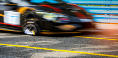 电动机体育运动车赛车沥青路与蓝色的栅栏和黄色的行交通标志车与快速度开车和运动模糊黑色的赛车车与红色的和黄色的条纹车赛马场