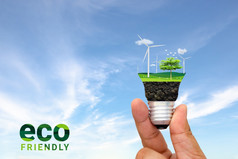 手持有光灯泡与风涡轮和树日益增长的绿色环境和生态友好的概念