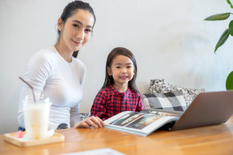 亚洲母亲是教学他们的女儿读书和使用<strong>笔记本电脑</strong>和技术为在线学习在学校假期<strong>首页</strong>教育概念和活动的家庭