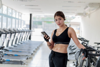 亚洲运动员运动服装时尚服装女运动员听音乐使用电话应用程序为健身活动跟踪器心率监控跟踪她的健康进步智能手机
