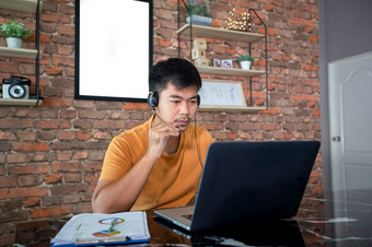 亚洲商人使用笔记本电脑和穿耳机为在线会议和工作从首页