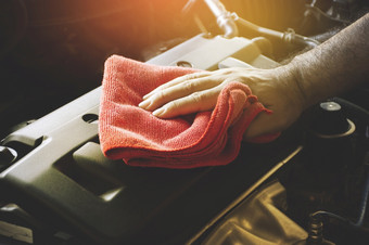人类手擦拭车引擎封面与红色的超细纤维布