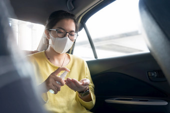 亚洲女乘客绿色黄色的衬衫和保护面具喷涂消毒液酒精她的手掌和她的手为防止冠状病毒冠状病毒而她的车清洁防腐剂卫生健康的和健康哪概念