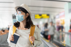 快乐亚洲女人穿保护脸面具和眼镜走国际机场终端在病毒流感大流行微笑年轻的女旅行者与黄色的背包的离开大厅