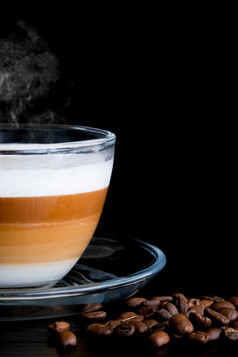 特写镜头裁剪透明的玻璃杯卡布奇诺咖啡与可见层咖啡牛奶和泡沫和咖啡豆子黑色的木表格咖啡馆黑暗场景的地方为文本烟垂直图像