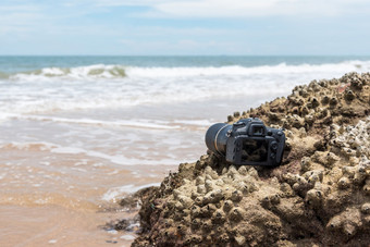 数码单反相机相机与长焦镜头湿从水海波石头海滩当旅行和测试使用的极端的环境演示防水摄影师数码单反相机相机石头海滩湿从水海波