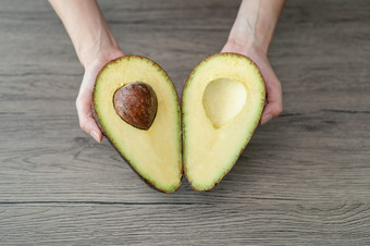 女人手持有减少一半切片新鲜的绿色鳄梨棕色（的）木表格水果健康的食物概念