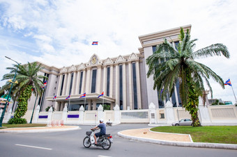 高棉语人骑摩托车通过的皇家政府大厅柬埔寨阳光明媚的一天的第一个现代政府建筑后的民事战争金边在金边城市