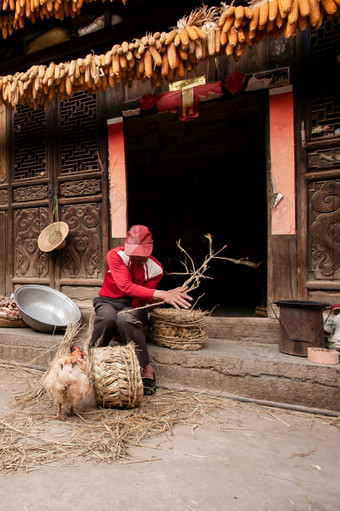 云南中国3月中国人老男人。使玉米椅子前面老迷人的中国人房子美丽的艺术木纹理玉米干燥挂在的通过公鸡前景chengzi村