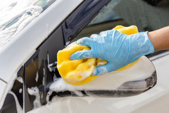 女人手穿蓝色的手套与黄色的海绵洗一边镜子现代车清洁汽车车洗概念