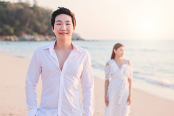 年轻的快乐亚洲夫妇的海滩与男人。面对的相机鼓浪漫的旅行度蜜月假期夏天假期亚洲女人和男人。持有手拥抱在户外